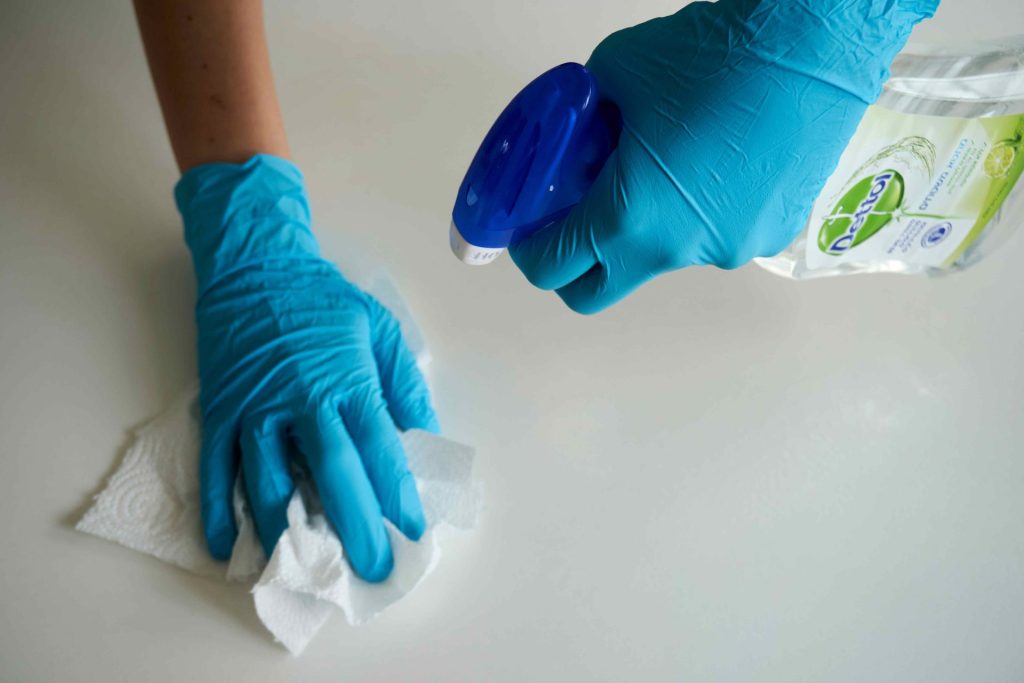 Gloved hand wiping surface with disinfectant spray