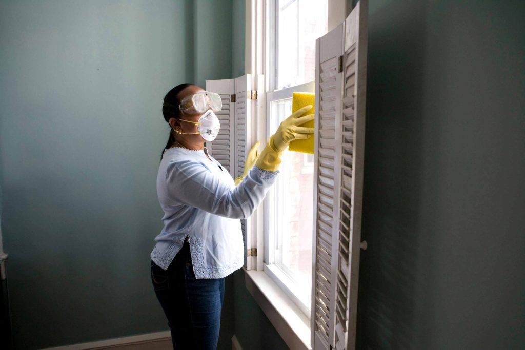 Woman cleaning window shutters while masked