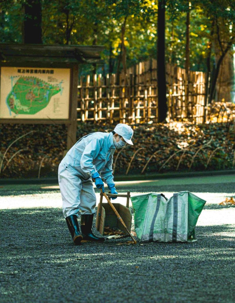 Worker raking leaves into large green bags